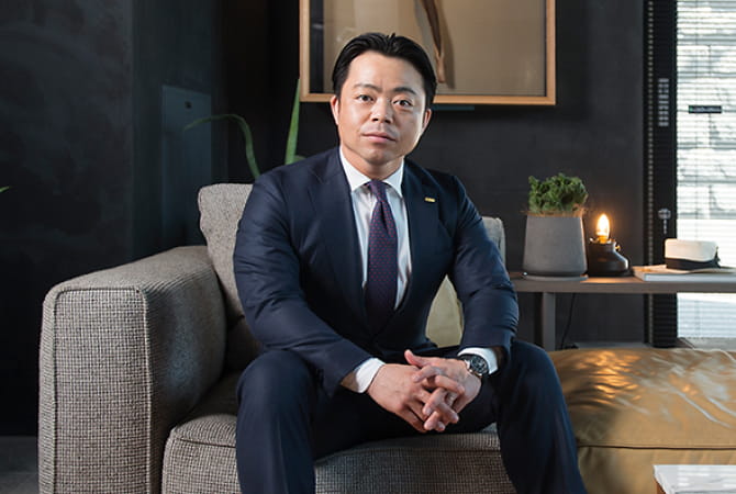 スーツ姿の男性がソファに座るポートレート写真で、信頼感や専門性を印象づける構図になっている