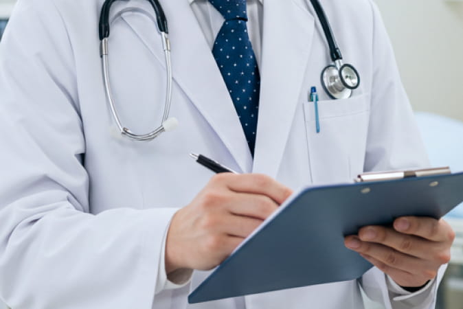白衣を着た医師が、聴診器を首にかけながらクリップボードに記入している様子